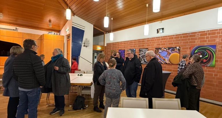 Menschen in einem Raum, der mit Kunstwerken dekoriert ist, stehen in Gruppen zusammen.