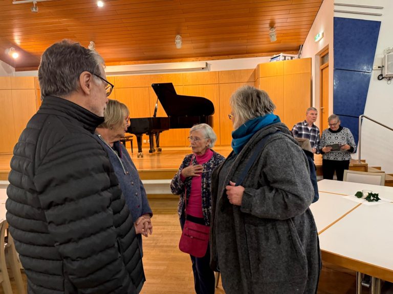 Vier Personen unterhalten sich in einem Raum mit einem Piano im Hintergrund.